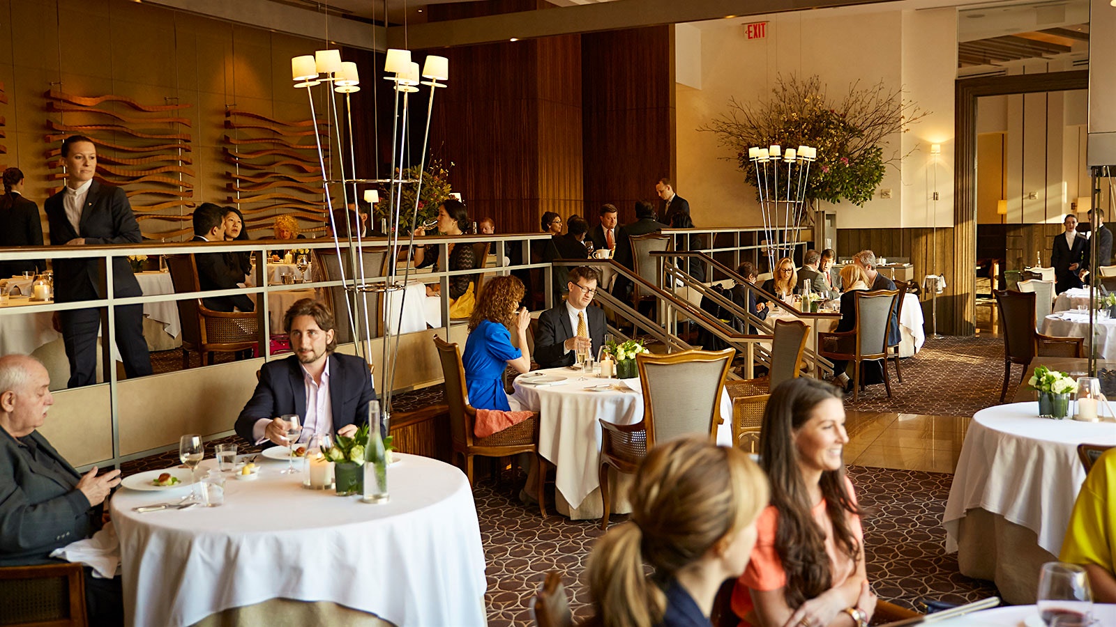 Guests dining in the dining room at Per Se, with Louis XV–style chairs, gold furnishings and tall, thin modern lights coming up from the floor